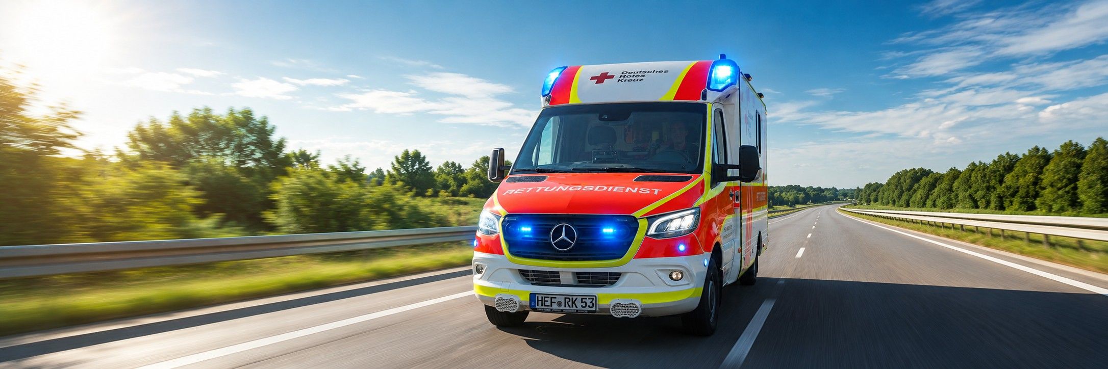 Foto: Zu sehen ist ein DRK-Rettungswagen von vorne in schneller Fahrt. Fahrer und Beifahrer konzentrieren sich auf die Fahrt.